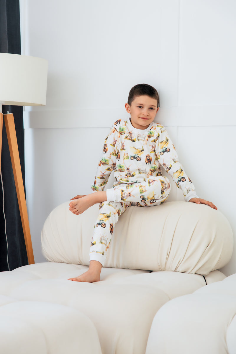 Soft cotton farm pyjamas showing Highland cows, sheep and tractors across rolling green fields.